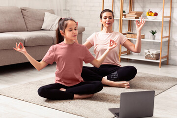 Home sports. Mother and daughter doing yoga or meditation while watching online tutorial on laptop indoors