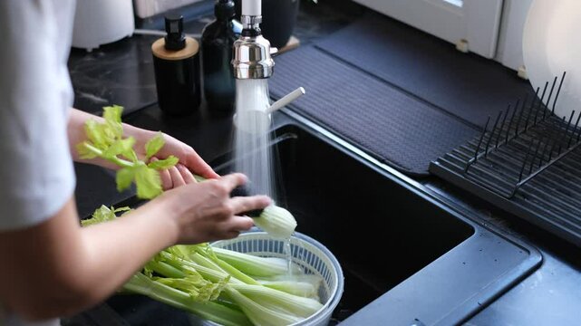 woman washes celery stalks close-up of hands