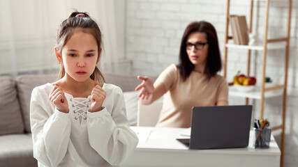 Lockdown family problems concept. Mother scolding upset daughter for hindering her online work at home