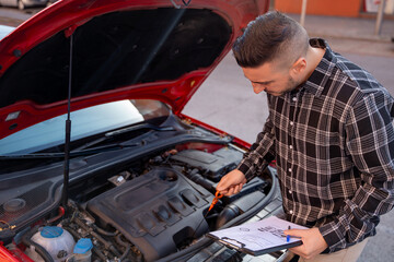 Insurance agent inspecting a car engine and completing paperwork after a road accident, assessing damage and filing an insurance claim