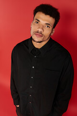 A young, handsome man in a stylish black shirt stands relaxed against vibrant red.