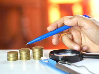 Hand holding pen pointing at coins on table. Saving money and financial business concept. Copy space.