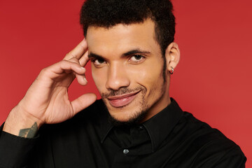 A young handsome man with a stylish look smiles confidently while posing against a red backdrop.