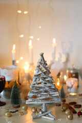 Various Christmas decorations, cookies, chocolate, nuts and tangerines, wine glasses and lit candles on the table. Holiday hygge at home. Selective focus.