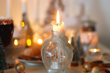 Various Christmas decorations, cookies, chocolate, nuts and tangerines, wine glasses and lit candles on the table. Holiday hygge at home. Selective focus.