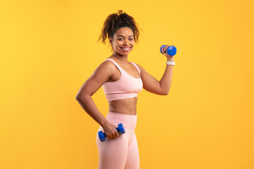 A woman in a pink workout outfit is lifting dumbbells against a vibrant yellow background. She appears confident and energized while engaging in a fitness activity, showcasing her strength.
