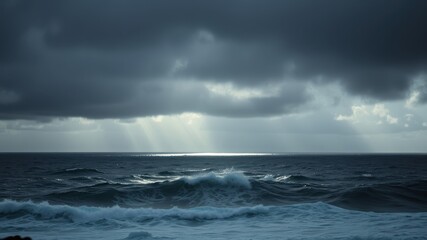 Rays of sunlight penetrate through a dense layer of stormy clouds, illuminating the restless ocean waves
