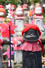 Stone Jizo statues at Zojoji Temple in Tokyo stand in rows, dressed in colorful hats and bibs. They...