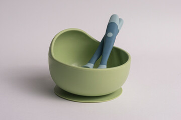 A green bowl with a silicone spoon and fork set for toddler feeding, isolated on a white background.