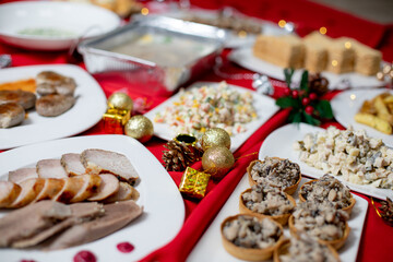 A festive plate of assorted sliced meats, including sausage and roast, served with sauce droplets on a white plate against a decorated red tablecloth.