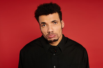 A young handsome man stands in front of a bright red background with a serious expression.