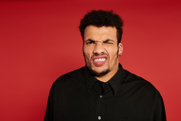 A handsome young man poses playfully with a silly expression in a vibrant studio.