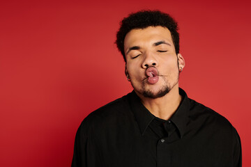 Young man with a charming smile and playful expression stands against a bold red backdrop.