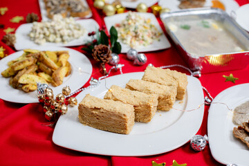 Slices of layered honey cake (Medovik, Napoleon) with a golden crumb coating served on a festive table with holiday decorations and a red tablecloth.
