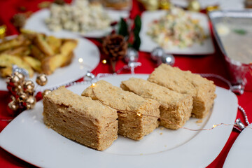 Slices of layered honey cake (Medovik, Napoleon) with a golden crumb coating served on a festive table with holiday decorations and a red tablecloth.
