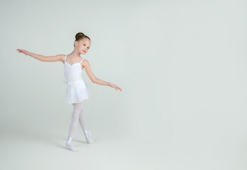 Fototapeta premium A little adorable young ballerina poses on camera. Ballet school concept. Studio portrait