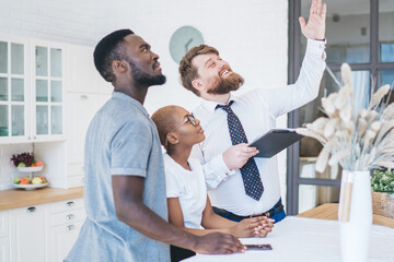 Obraz premium Attentive ethnic couple and real estate agent inspecting ceiling in new apartment