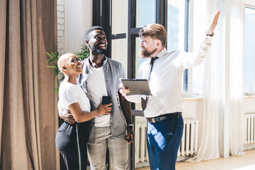 Multiethnic couple looking around new flat with realtor