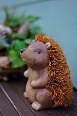Decorative Hedgehog on a Wooden Table. A charming hedgehog figurine made of natural materials sits on a wooden table against a background of green branches. Warm and cozy rustic atmosphere.
