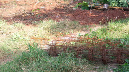 Rolls of old wire mesh are rusted and brown. Vacant on an area with tall grass. Construction material concept