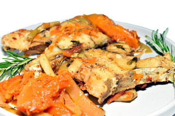 Cod fish with vegetables and herbs, ready to eat, lies on a plate, side view. Close-up.