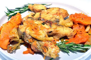 Cod fish with vegetables and herbs, ready to eat, lies on a plate, side view.
