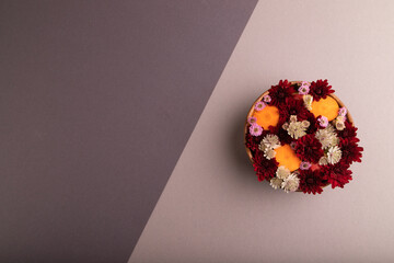 wooden bowl with carrot slices and red Chrysanthemum flowers, Astrantia flowers, flower salad on beige and gray pastel paper, top view, copy space
