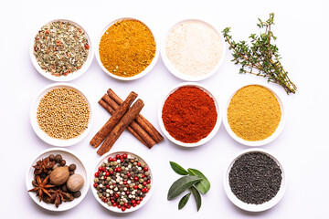 Bright set of aromatic organic spices and herbs such as smoked paprica, peppercorn, thyme, bay leaf, curry, dry garlic and others on white background top view.