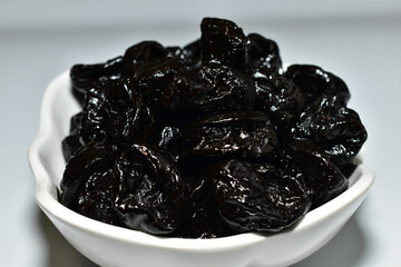 Dried prunes lie in a deep plate. Close-up. Side view.