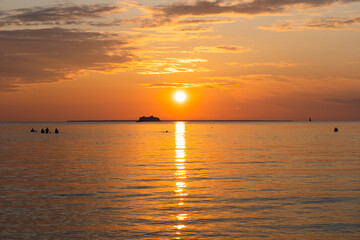Obraz premium Estonia. People are stand in the sea with ferry sailing in the distance at sunset.