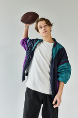 In a modern studio, a young man exudes style and confidence while holding a football.