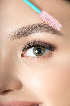 Young beautiful brunette girl with natural makeup and laminated brows holds brush for eyebrow corrections. Eyebrow correction and perm lamination procedure. Close-up, selective focus.