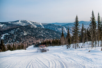 Landscape snowy mountains, mountain range in haze winter. Snowcat removes snow