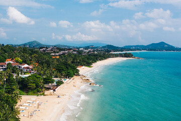 Aerial scenery view of white sand shore with turquoise clear sea water. Bird's eye panoramic view of picturesque lagoon with hotels on beach. Populated island in Thailand