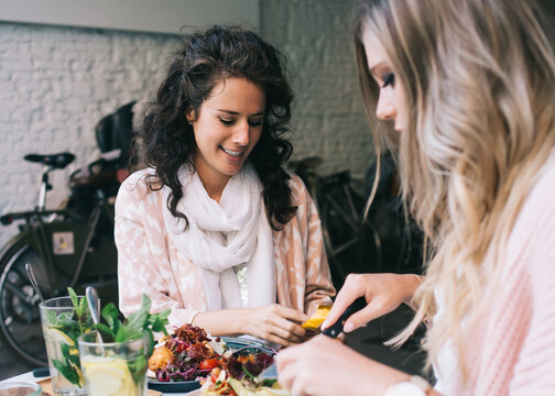 Smiling caucasian female colleagues spending free time on dinner together eating healthy meal and talking to each other, positive women 20s enjoying lunch break and delicious food on leisure