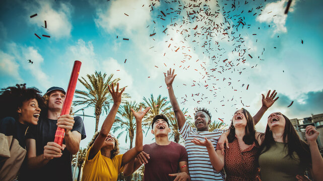 Group of friends enjoying party throwing confetti in the air - Multicultural young students having fun celebrating and laughing out loud outdoors - Youth, friendship and summertime concept