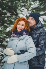 Obraz premium Love romantic love story. Happy couple of middle aged millennials, bright red-haired woman in winter snow park. Romantic date, kissing, hugging. Walking, having fun. Stylish blue clothes, jacket, hat