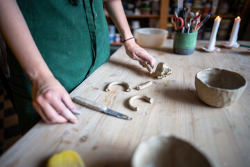 Female potter hands selecting handle for clay mugs on table, cutting and shaping clay. Refining pottery details, preparing for assembly. Workspace in ceramic studio for final stages of creation