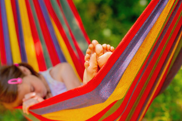 Portrait of young beautiful girl resting and sleeping in comfortable hammock at green garden. Selective focus on bare feet. Horizontal image.