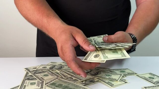 A person is carefully collecting and counting a large amount of cash spread across a table. The setting is bright and organized, focusing on the activity of managing money.