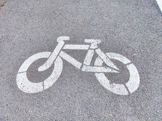 Street mural of a bicycle symbol painted on an asphalt pathway in a city during daylight hours