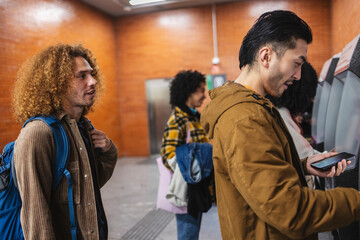 Fototapeta premium Young tourists using mobile phone to buy train tickets at station