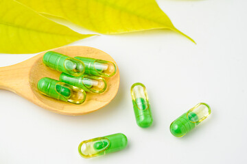 transparent capsules pills with a mixture of green powder and oil in wooden spoon, vitamin supplements