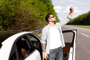 Stressed millennial Caucasian guy standing near car with cellphone, having problem, trying to find mobile network, having no signal to call breakdown service. Road emergencies, no phone connection