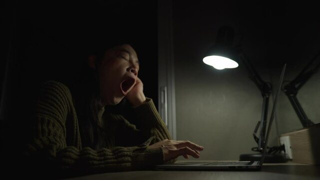 sleepy woman yawning while working with laptop at night