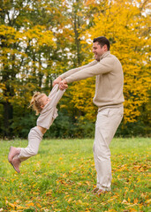 Joyful dad circles his young daughter in autumn park. All around is bright carpet of yellow leaves. Child is laughing. Concept: fathers love, happy childhood, happy family.