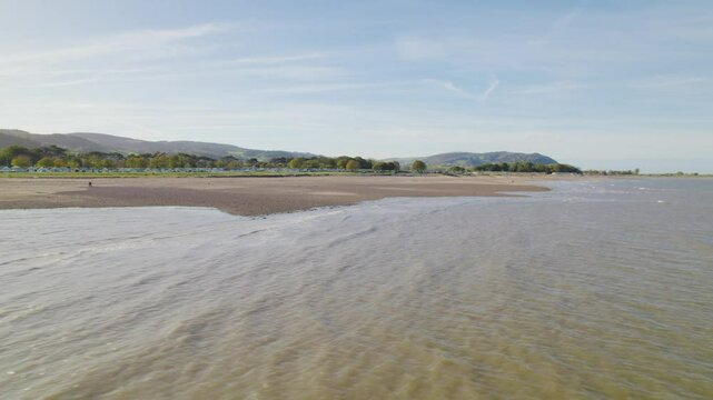 view of calm sea and Dunster Beach is empty on a sunny day with trees and cliffs in the background