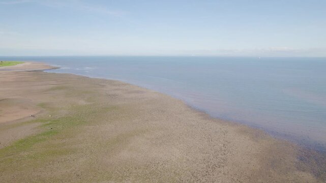 Aerial scenery of a sandy coastline meets blue waters under clear sky in Dunster Beach, Somerset, UK