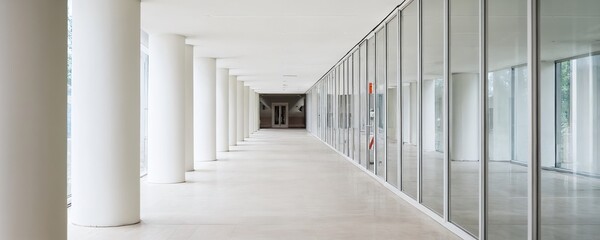Wide corridor featuring glass walls and columns in a modern architectural setting during daylight