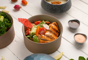Healthy caesar salad with grilled chicken steak, white wood background